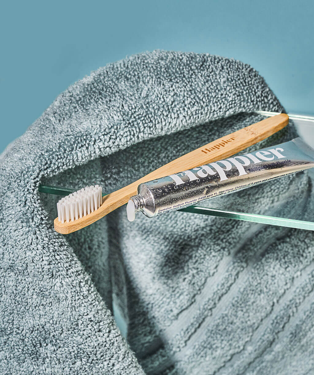 A toothbrush and toothpaste placed on a towel, including Happier Fresh Mint Toothpaste Travel Size 20ml.
